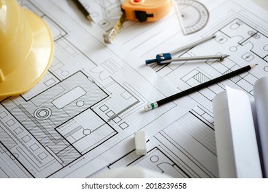 Yellow hard safety helmet hat and architectural blueprints and blueprint rolls and pencils pen, ruler, protractor, and tape measure on the table at the construction site. - Shutterstock ID 2018239658