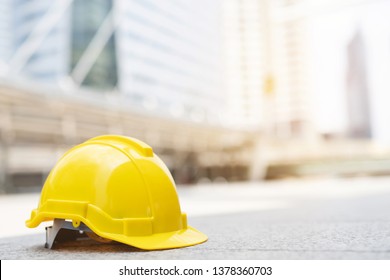 Yellow Hard Safety Wear Helmet Hat In The Project At Construction Site Building On Concrete Floor On City With Sunlight. Helmet For Workman As Engineer Or Worker. Concept Safety First. 