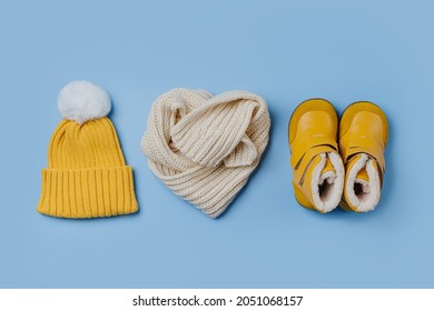 Yellow hat and boots with scarf on blue background. Stylish childrens outerwear. Winter fashion outfit 