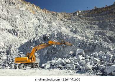 Yellow hydraulic breaker, on a wheelbase, breaks a large fragment of limestone at the bottom of a stone quarry, close-up. - Shutterstock ID 2164441605