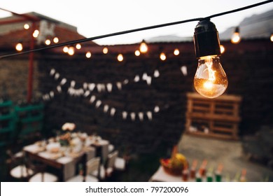 Yellow Lamp Hangs Over Dinner Tables Outside