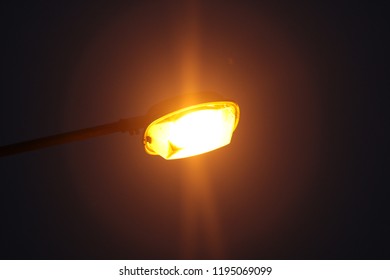 Yellow Lamp Post Close Up Bulb . Black Background At Night .