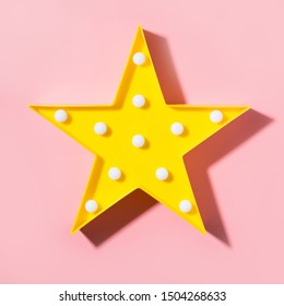 Yellow lamp as star with white LED lights with shadow on pastel pink background. Creative minimal concept. Top view. Flat lay style. Children's modern night light. Square image.