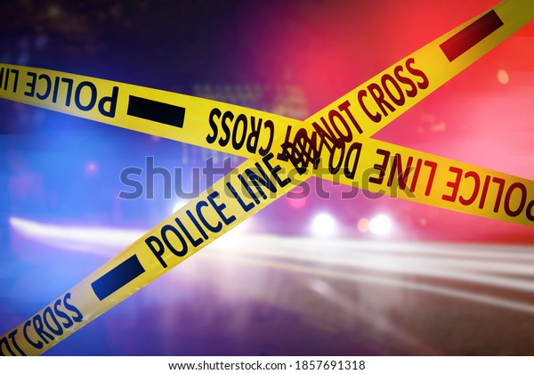 Yellow\
law enforcement tape isolating crime scene. Blurred view of city\
street, toned in red and blue police car\
lights