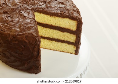 A Yellow Layer Cake With Chocolate Icing With A Slice Missing