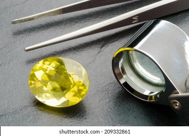 Yellow lemon quartz gemstone with tweezers and loupe on black stone plate.