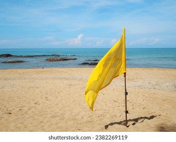 The yellow life saving flags on flagpole flutters in the wind against blue sky,  Flag and shadow on the sand. Yellow flag is planted on the beach as a warning sign about safety when swimming - Powered by Shutterstock