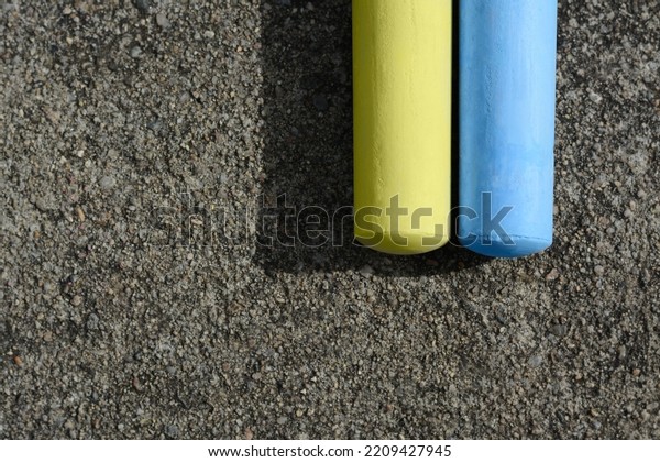 Yellow and light blue chalk sticks on asphalt, flat\
lay. Space for text