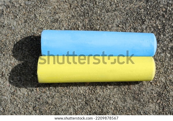 Yellow\
and light blue chalk sticks on asphalt, flat\
lay