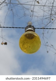 Yellow lightbulb on a wire under a cloudy blue sky - Shutterstock ID 2311494697