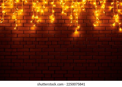 Yellow lights garlands hanging from red brick wall at evening, beautiful christmas house decoration with magic holiday atmosphere. Festive Christmas garlands with luminous yellow light on wall - Powered by Shutterstock