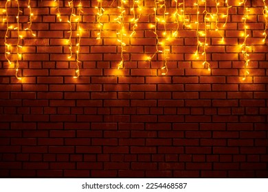 Yellow lights garlands hanging from red brick wall at evening, beautiful christmas house decoration with magic holiday atmosphere. Festive Christmas garlands with luminous yellow light on wall - Powered by Shutterstock