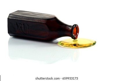 Yellow liquid pours out from brown faceted bottle on slightly reflective surface