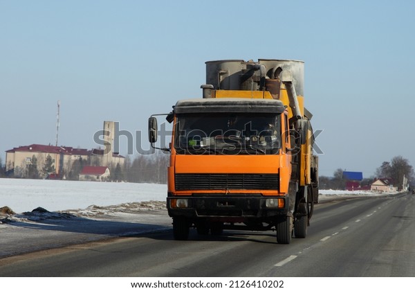 Yellow loaded small\
truck on suburban winter road in Europe. Front view closeup.\
Transportation\
logistics.