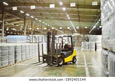 Yellow loader on the background of a huge industrial food warehouse with plastic PET bottles with beer, water, drinks.