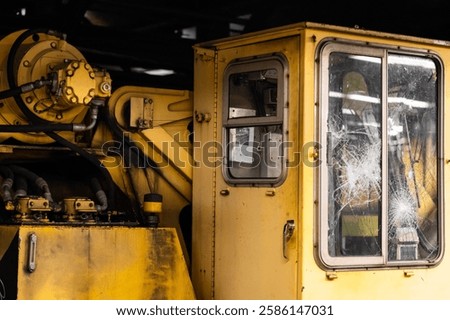 A yellow machine with a broken window. The window is covered in glass and the machine is in a dirty, rundown state