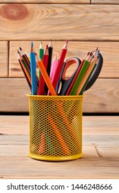 Yellow metal holder with multicolored pencils. Stationery supplies on wooden background. Concept of education.