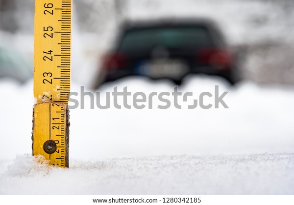 Yellow meter rule is stuck in a snow\
with car in background in winter in Bavaria,\
Germany