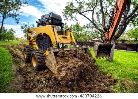 Yellow mini bulldozer working with earth, moving soil and doing landscaping works