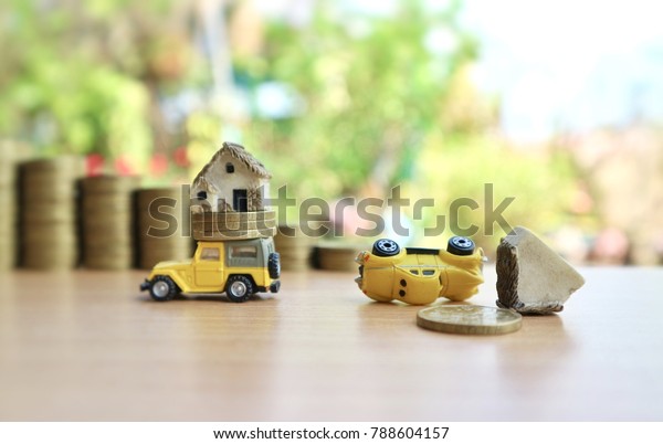 Yellow miniature car carry coins and house with vehicle\
falls on wood table in blur roll ladder of gold money in natural\
tree bright light, success and failure concept                     \
         