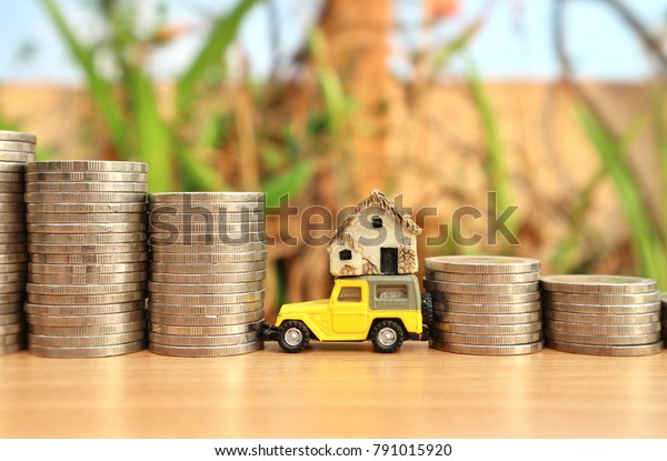 Yellow\
miniature car carry tiny house between roll ladder of coin money on\
wood table in blur natural tree                  \
