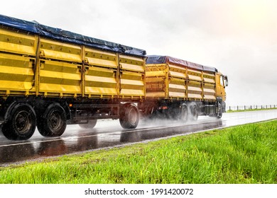 Yellow modern grain truck transporting grain in rainy weather on the highway, in the background. Slippery road, agribusiness