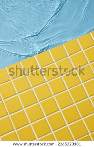 Yellow mosaic tiles background with blue water for summer concept. Blank space. Top view