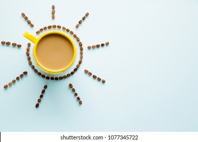 Yellow mug of coffee with milk on light pastel blue table from above. Wake up with morning coffee. Sun created from brown beans. Empty place for inspirational, motivational text or quote.  Top view.
