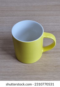 A yellow mug with a white interior stands on a light brown desk against a soft gray background. The simple yet elegant composition showcases the combination of colors and textures. - Shutterstock ID 2310770531