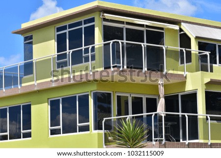 Yellow multi-story holiday house with verandas protected by glass railing and tinted glass windows.