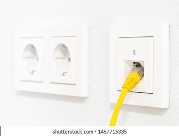 Yellow Network Cable In Wall Outlet For Office Or Private Home Lan Ethernet Connection With Power Outlets Flat View On White Plaster Wall Background - Selective Focus