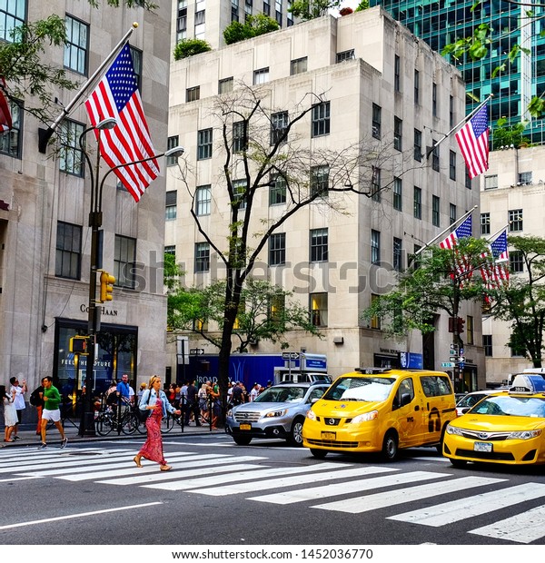 Yellow New York City taxi cabs are waiting for\
the pedestrian to cross the road on Fifth Avenue in Manhattan.\
Manhattan, New York, USA - June 15,\
2018