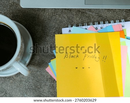 Yellow note with Black Friday message and hearts beside coffee mug and colorful sticky notes on wooden desk creating lively and casual workspace atmosphere.