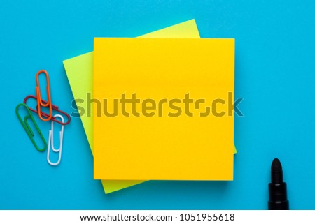 Yellow note with empty place for your text with marker and paper clips on blue background. Reminder concept.