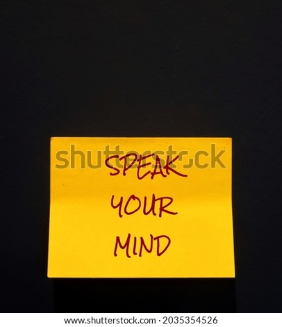 Yellow note on copy space black wall with text handwriting SPEAK YOUR MIND, self reminder to be true to yourself, express feelings or opinions frankly , say what you think without fear