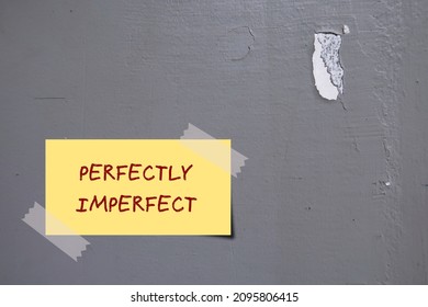 Yellow note on gray wall with handwritten text PERFECTLY IMPERFECT, concept of accept yourself no matter what, with all flaws, imperfections make life interesting and help us grow
