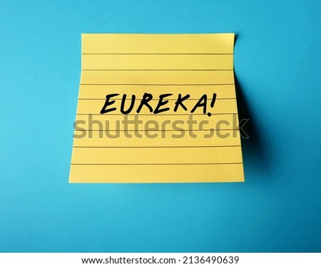 Yellow note pad on blue background with handwritten text EUREKA! means 