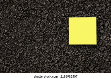 Yellow Note Paper Square On Black Soil Texture Ground Close Up. Yellow Sticky Note Blank Paper Flat Soil Organic Earth Texture. Mockup On Ground Soil Background Top View From Above. Humus. Agriculture