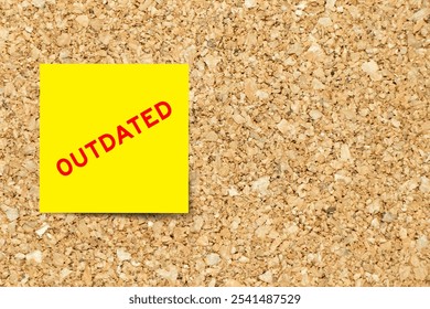 Yellow note paper with word outdated on cork board background with copy space