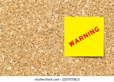 Yellow note paper with word warning on cork board background with copy space - Shutterstock ID 2207070813
