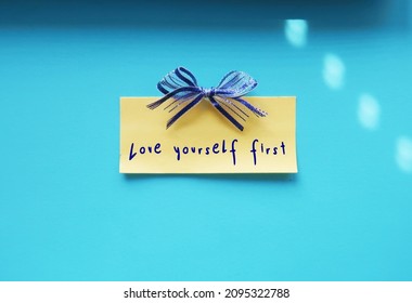 Yellow Note With Ribbon On Blue Wall With Handwritten Text LOVE YOURSELF FIRST, Concept Of Self Talk Affirmation, Reminder To Love And Respect Yourself First Before Loving Others