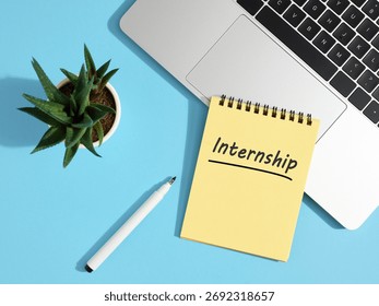 Yellow notepad with internship handwritten message, placed near laptop and pen on blue office desk