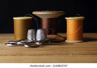 YELLOW OCHRE COTTON REELS WITH SCISSORS AND TWO THIMBLES AND OLD VINTAGE WOODEN SPOOL AND THREAD IN BACKGROUND