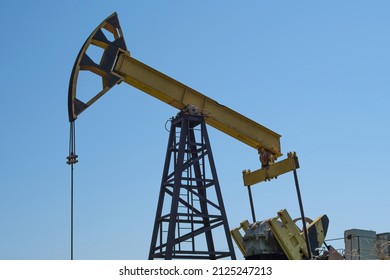 A Yellow Oil Rig Pumping Oil Against A Blue Sky. Extraction Of Black Gold From The Well