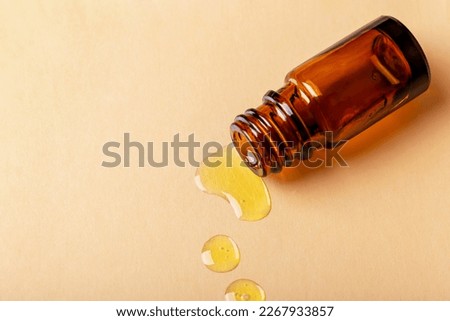 Yellow oil spilled from the cosmetic amber bottle. Beige background with copy space