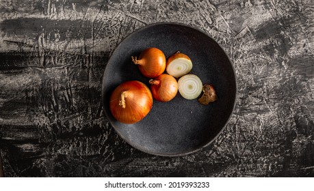 Yellow onions on a dark plate. Minimalistic background with vegetables.