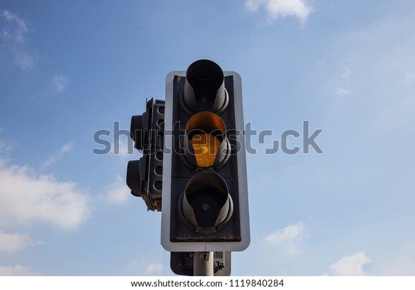 Yellow, orange color\
traffic light isolated. Blue sky with few clouds background. Close\
up under view.
