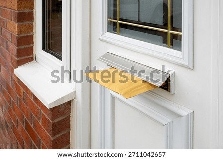 Yellow padded envelope from online shopping lodged in a house letterbox with a metal flap on a white front door. Concept of mail delivery, postage, online shopping, and home correspondence