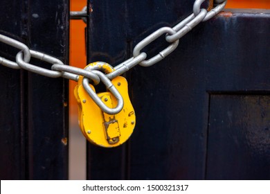 Yellow Padlock With Chain Locking A Black Wooden Gate