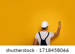 Yellow paint. Close-up photo of the man in a working suit and white helmet, who is painting a wall in yelllow.